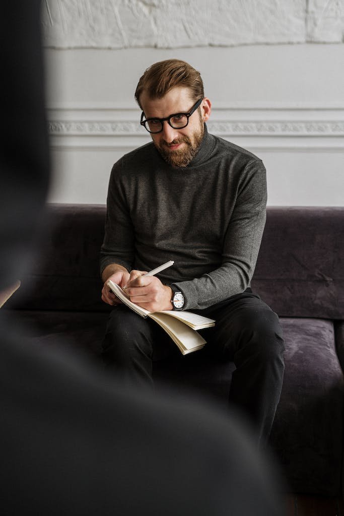 Man in Gray Sweater and Black Pants Sitting on Purple Couch